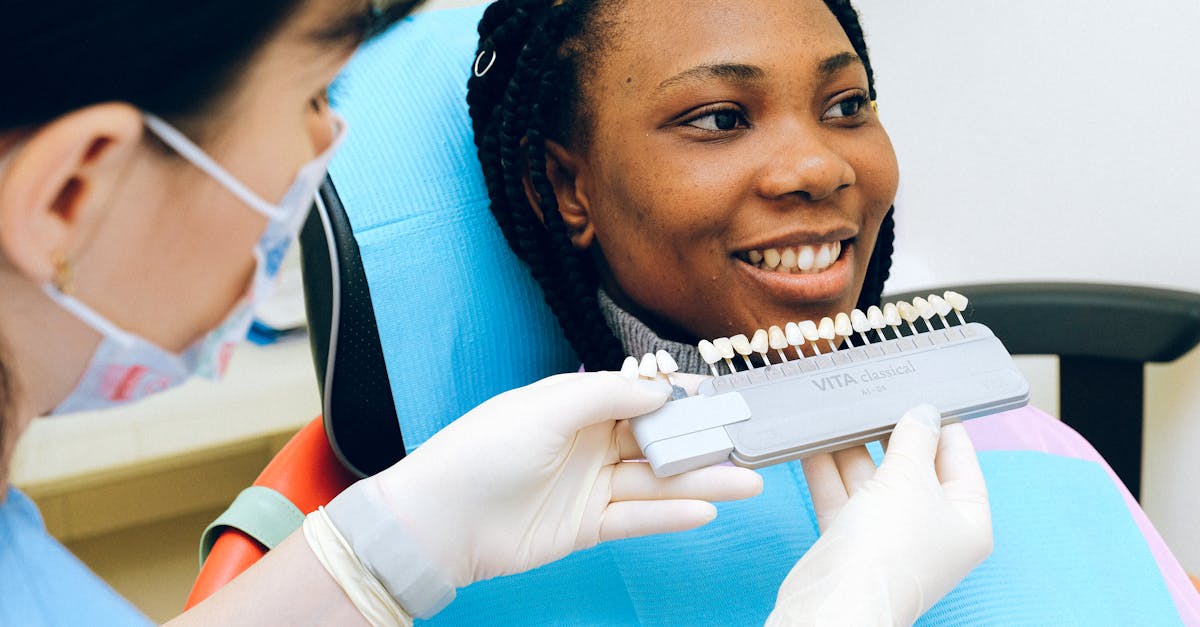 cheerful black woman sitting in dental chair of modern dentist office and checking teeth implant whi